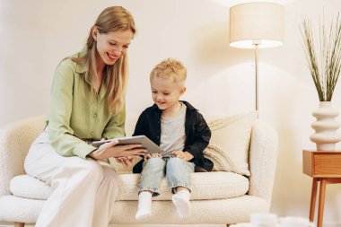 Kadın oğluyla oturuyor ve tablet kullanıyor.