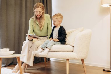 Kadın oğluyla oturuyor ve tablet kullanıyor.