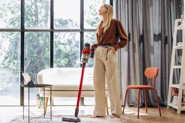Ev işi yapan ve kablosuz elektrik süpürgesi kullanan bir kadın.