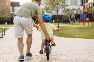 Baba küçük oğluna bisiklet sürmeyi öğretiyor.