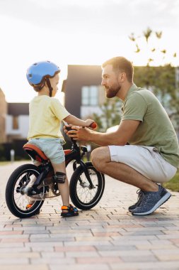 Baba küçük oğluna bisiklet sürmeyi öğretiyor.