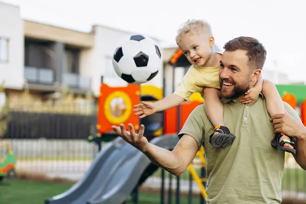 Father with son holding football ball and having fun at the playground
