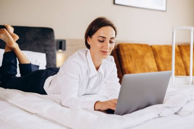 Yatakta yatan ve otel odasında bilgisayarla çalışan bir iş kadını.