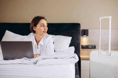 Yatakta yatan ve otel odasında bilgisayarla çalışan bir iş kadını.