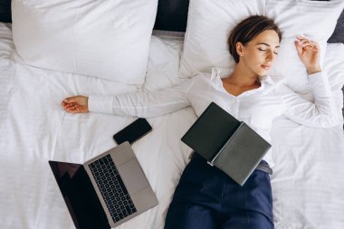 İş kadını otel odasında dizüstü bilgisayarı ve telefonu yatakta yatıyor.