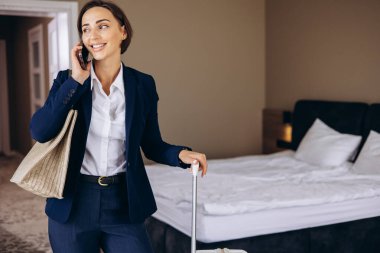 Otel odasında konuşan ve bavullarını taşıyan bir iş kadını.