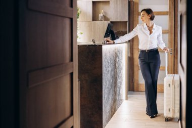 Otel resepsiyonunda bavullu bir iş kadını.