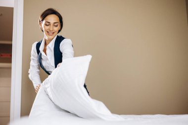 Kadın hizmetçi otel odasında yatak örtüsü hazırlıyor.