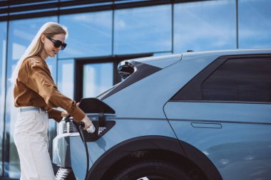Kadın elektrikli arabaya elektrik kablosu takıyor.