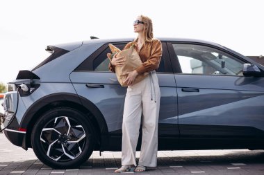 Elektrikli araba şarj edilirken alışveriş yapan kadın.