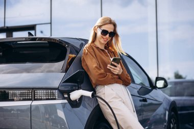 Elektrikli arabasının yanında telefonla konuşan bir kadın.