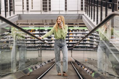 Yürüyen merdivendeki kadın malzeme deposunda telefonuyla konuşuyor.