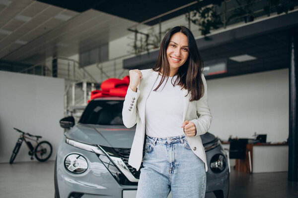 Женщина счастлива, стоя рядом со своей новой машиной в автосалоне