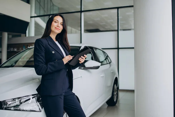 Sales woman with tablet in a car showroom standing by white car