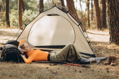 Ormanda çadırın yanında sırt çantasına uzanmış bir kadın.