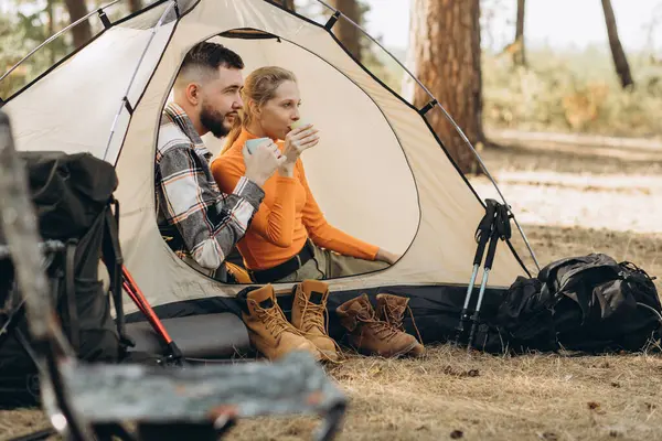 森で紅茶を飲むテントで一緒に座っている旅行者のカップル — ストック写真