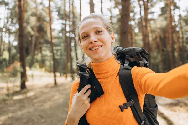 stock image Woman hiking with bag and walking sticks in forest making selfie