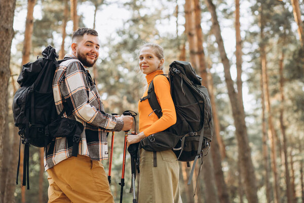 Couple hiking with bags and walking sticks in forest