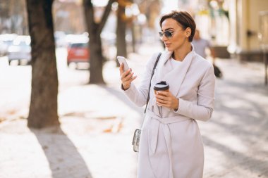 Telefonlu bir iş kadını sokakta kahve içiyor.