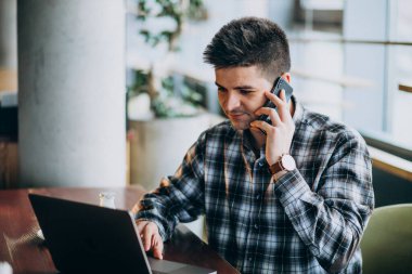 Genç yakışıklı iş adamı bir kafede dizüstü bilgisayar kullanıyor.