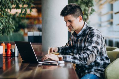 Genç yakışıklı iş adamı bir kafede dizüstü bilgisayar kullanıyor.