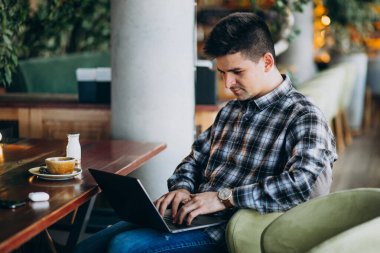Genç yakışıklı iş adamı bir kafede dizüstü bilgisayar kullanıyor.