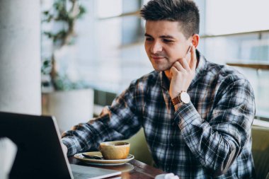 Genç yakışıklı iş adamı bir kafede dizüstü bilgisayar kullanıyor.