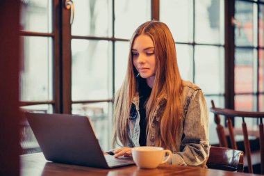 Dizüstü bilgisayarda çalışan ve barda kahve içen genç bir kadın.