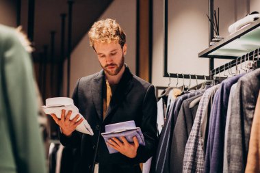 Genç yakışıklı bir adam dükkanda gömlek seçiyor.