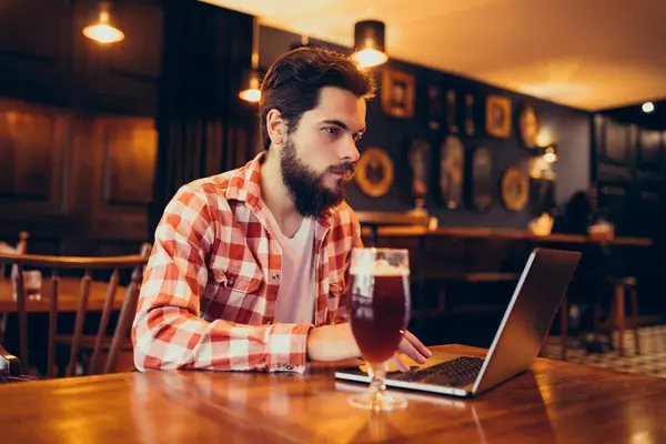 Youn g bearded man working on laptop in a bar