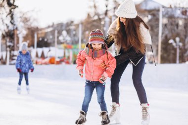 Anne ve kızı buz pateni pistinde paten öğretiyor.