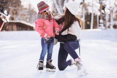 Anne ve kızı buz pateni pistinde paten öğretiyor.