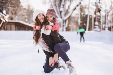 Anne ve kızı buz pateni pistinde paten öğretiyor.