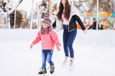Anne ve kızı buz pateni pistinde paten öğretiyor.