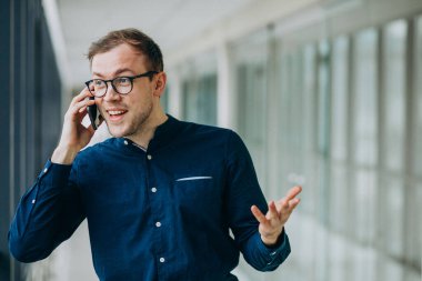 Genç yakışıklı adam ofiste telefonla konuşuyor.