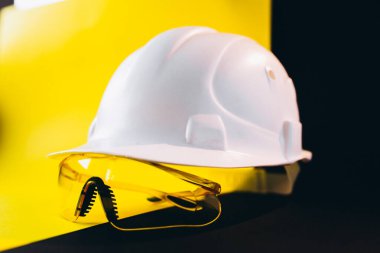 Siyah ve sarı arka planda izole edilmiş koruyucu gözlüklü beyaz şapka.