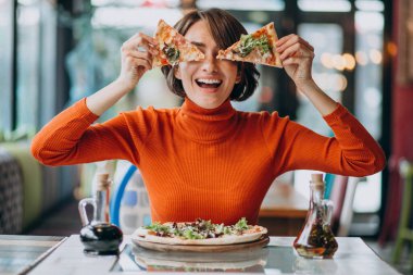 Pizzacıda pizza yiyen genç ve güzel bir kadın.