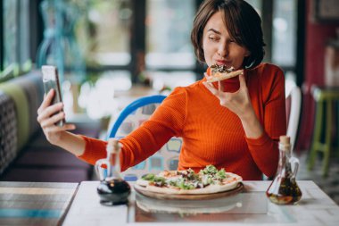 Pizzacıda pizza yiyen genç ve güzel bir kadın.