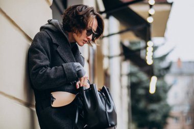 Caddenin dışında gri paltolu güzel bir kadın var.