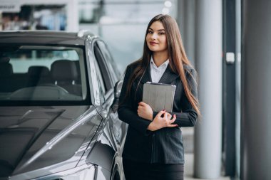 Araba galerisindeki genç bayan arabanın yanında duruyor.