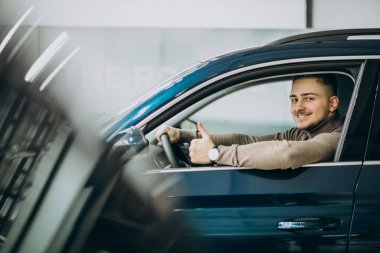 Genç yakışıklı bir adam araba galerisinde araba seçiyor.