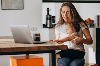Küçük oğluyla birlikte laptopta çalışan genç bir anne.