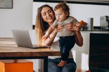 Küçük oğluyla birlikte laptopta çalışan genç bir anne.