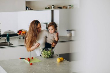 Genç anne ve küçük oğlu mutfakta salata yapıyor.