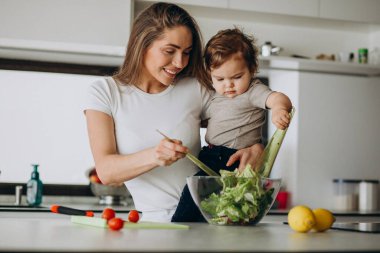Genç anne ve küçük oğlu mutfakta salata yapıyor.