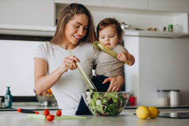 Genç anne ve küçük oğlu mutfakta salata yapıyor.