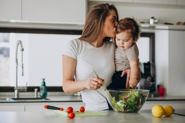Genç anne ve küçük oğlu mutfakta salata yapıyor.