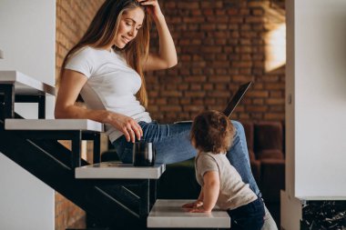 Küçük oğluyla birlikte laptopta çalışan genç bir anne.