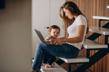 Küçük oğluyla birlikte laptopta çalışan genç bir anne.