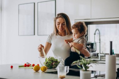 Genç anne ve küçük oğlu mutfakta salata yapıyor.
